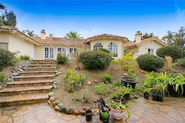 rear view of house featuring a tiled roof, stucco siding, a patio, and a chimney