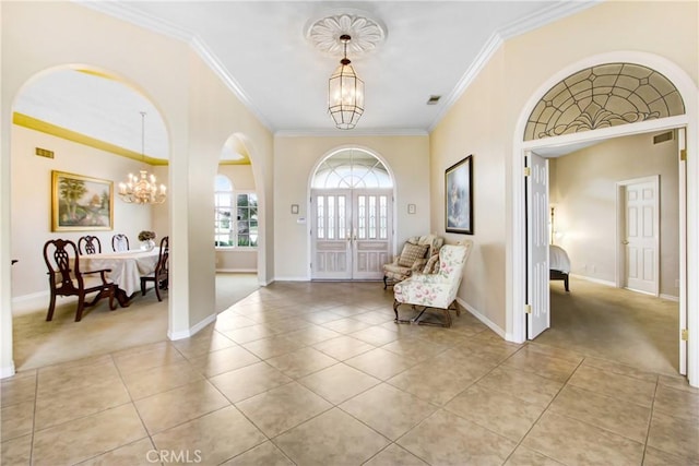 entrance foyer with baseboards, a chandelier, crown molding, light tile patterned flooring, and light colored carpet