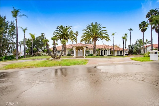 mediterranean / spanish-style home with a front lawn, curved driveway, stucco siding, and a tile roof