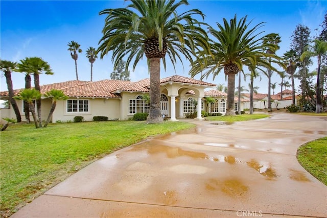 mediterranean / spanish-style home with stucco siding, a tiled roof, and a front lawn