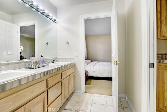 ensuite bathroom featuring double vanity, a sink, baseboards, and connected bathroom