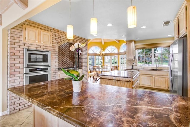 kitchen featuring a kitchen island, light brown cabinetry, a wealth of natural light, and stainless steel appliances