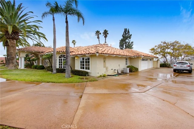 view of side of home featuring concrete driveway, stucco siding, an attached garage, a tile roof, and a yard