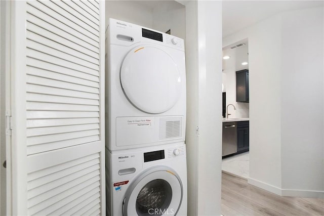 1400 Pacific Coast Unit 305, Huntington Beach, CA 92648 - laundry area featuring a sink, light wood-style floors, baseboards, stacked washer and clothes dryer, and laundry area