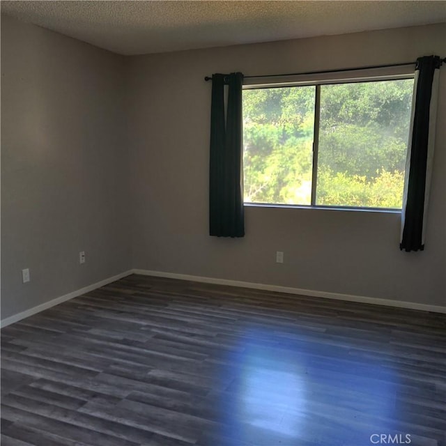 spare room with a textured ceiling, baseboards, and dark wood finished floors