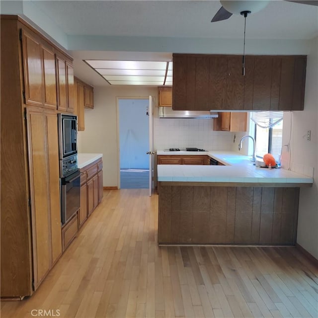 kitchen with backsplash, a sink, black appliances, light wood-style floors, and tile counters