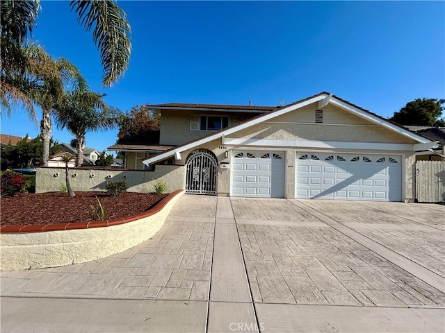 view of front facade with stucco siding, a gate, driveway, a garage, and fence