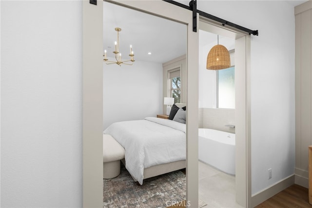 bedroom featuring a barn door, baseboards, an inviting chandelier, and wood finished floors