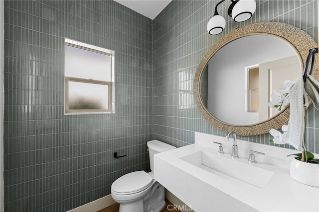 half bathroom featuring a sink, tile walls, and toilet