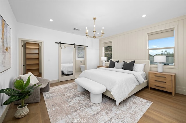 bedroom with light wood-type flooring, a notable chandelier, visible vents, and a barn door