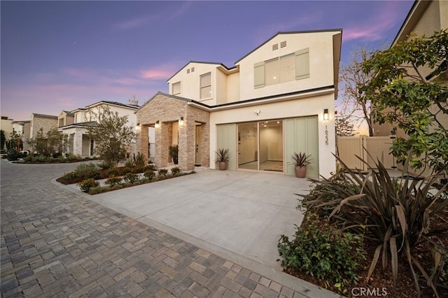 view of front of house with stone siding, stucco siding, and fence