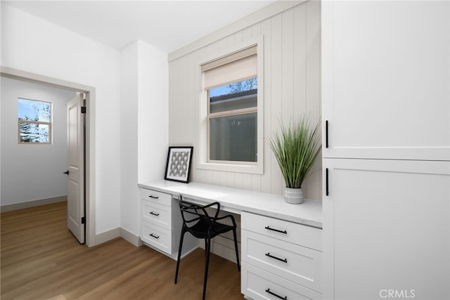 home office with built in study area, light wood-style floors, and baseboards