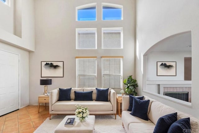 living area featuring light tile patterned floors, arched walkways, a healthy amount of sunlight, a towering ceiling, and a tiled fireplace