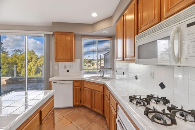 kitchen featuring tile countertops, light tile patterned floors, a sink, white appliances, and decorative backsplash