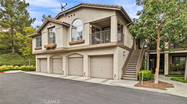 multi unit property with stairs, a garage, and stucco siding