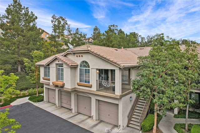 view of front of house with an attached garage, stucco siding, a tile roof, and stairway