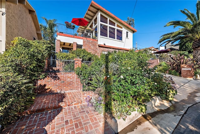 view of front of property featuring brick siding, fence, and a balcony