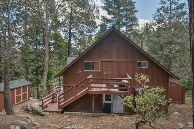 back of property with an outdoor structure, stairway, a shed, a deck, and a view of trees