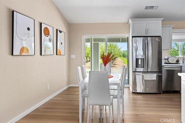 dining space with baseboards, light wood-style flooring, visible vents, and a healthy amount of sunlight