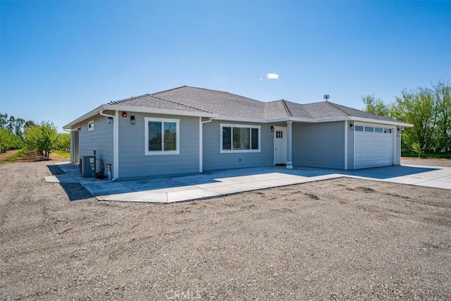 ranch-style house featuring a shingled roof, driveway, central air condition unit, and an attached garage