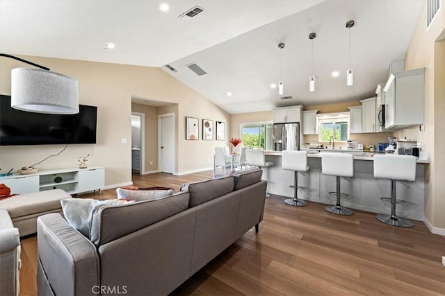 living area featuring wood finished floors, baseboards, lofted ceiling, and visible vents
