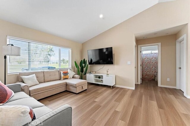 living area with baseboards, vaulted ceiling, and light wood-type flooring