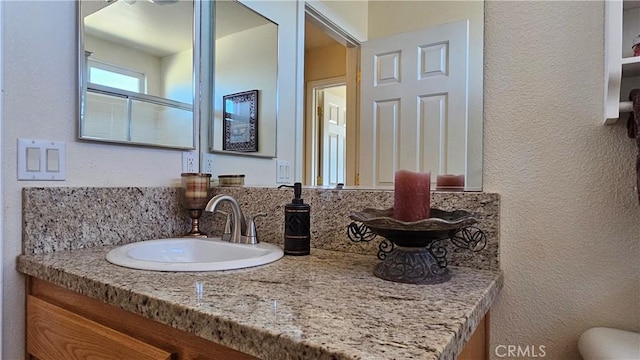 bathroom with a textured wall, vanity, and toilet