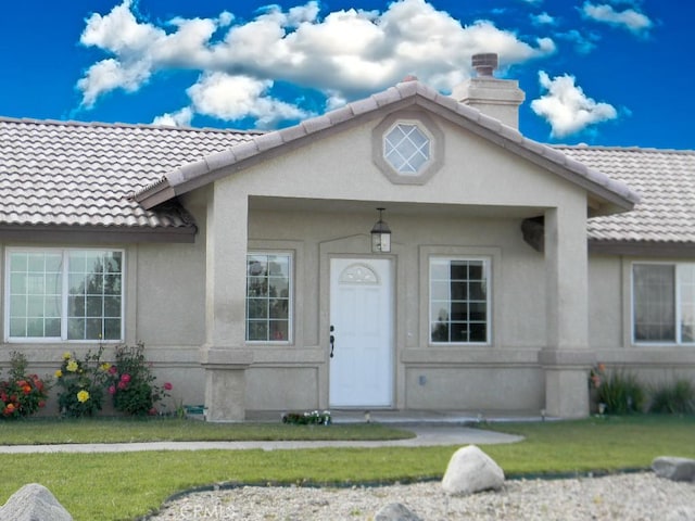 view of front of property with a chimney, stucco siding, a tile roof, and a front yard