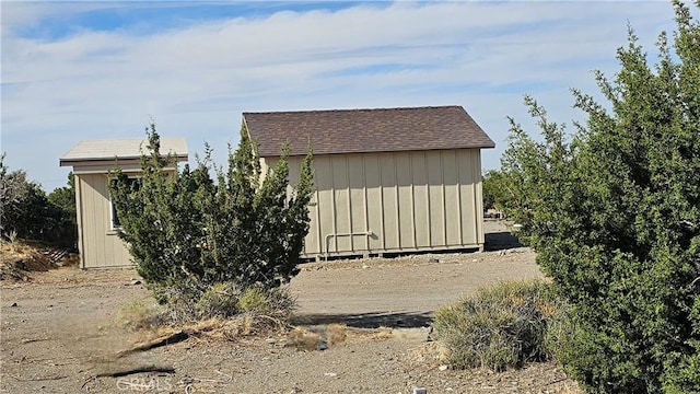 view of home's exterior with a shed, roof with shingles, and an outbuilding