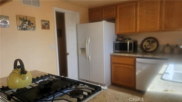 kitchen featuring white fridge with ice dispenser, visible vents, stainless steel microwave, light countertops, and dishwasher