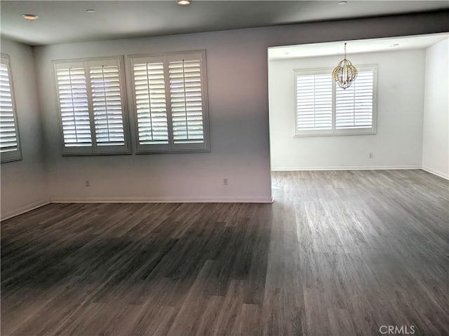 unfurnished room with baseboards, a notable chandelier, and dark wood finished floors