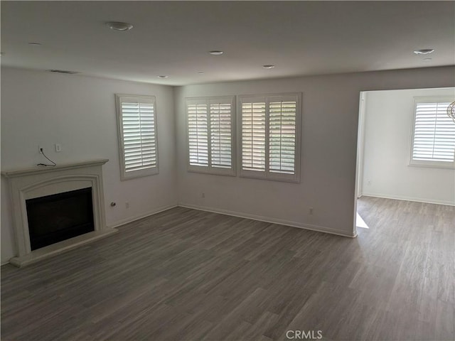 unfurnished living room with baseboards, visible vents, wood finished floors, and a fireplace with raised hearth