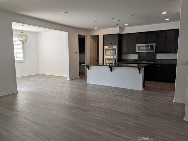kitchen featuring a chandelier, a kitchen island with sink, wood finished floors, stainless steel appliances, and a kitchen breakfast bar