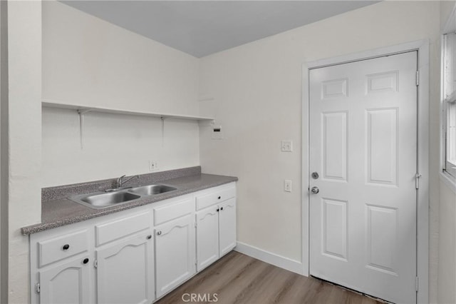 kitchen with baseboards, light wood finished floors, a sink, and white cabinets