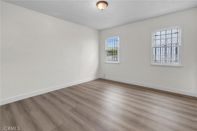unfurnished room featuring a textured ceiling, wood finished floors, and baseboards