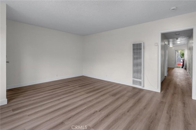 empty room with a textured ceiling, baseboards, a heating unit, and wood finished floors