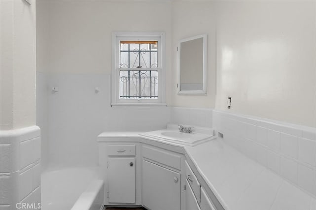 full bath featuring tile walls, vanity, washtub / shower combination, and a wainscoted wall