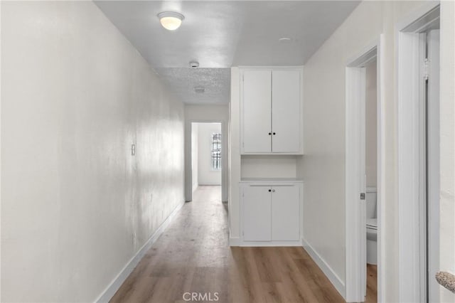 hallway with baseboards, light wood finished floors, and a textured ceiling