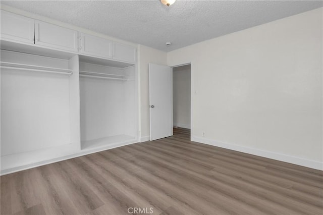 unfurnished bedroom with a textured ceiling, a closet, wood finished floors, and baseboards