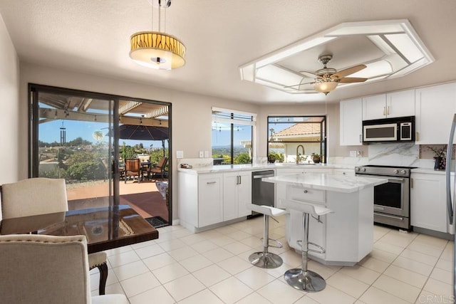 kitchen with stainless steel appliances, a ceiling fan, a kitchen island, a kitchen bar, and white cabinets