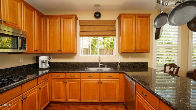 kitchen featuring brown cabinets, appliances with stainless steel finishes, a sink, dark stone counters, and dark wood-style floors