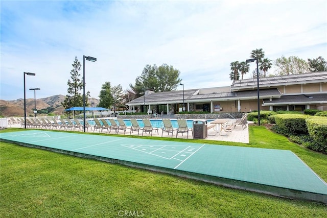 view of community featuring shuffleboard, a mountain view, a swimming pool, and a yard