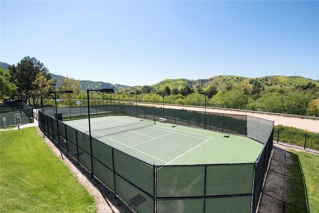 view of tennis court featuring a mountain view, fence, and a yard