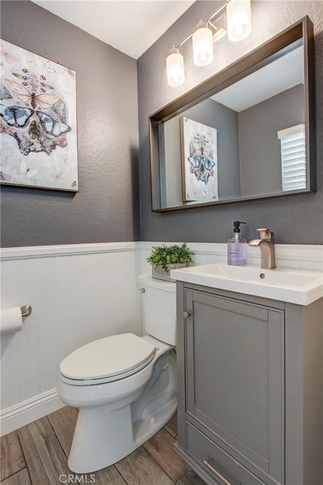 bathroom with wood finished floors, a wainscoted wall, toilet, and vanity