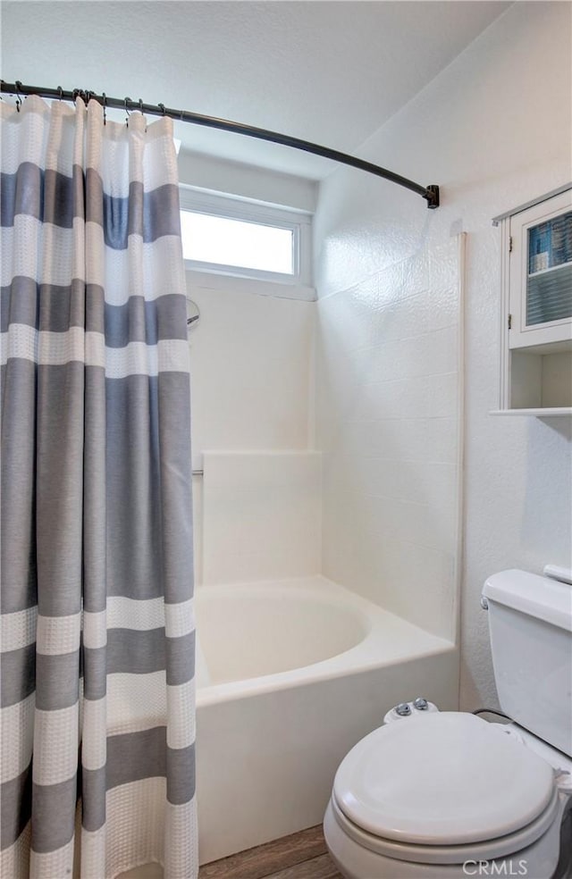 bathroom with shower / bathtub combination with curtain, wood finished floors, and toilet