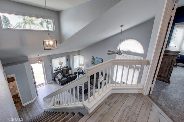 stairs with baseboards, high vaulted ceiling, wood finished floors, and ceiling fan with notable chandelier