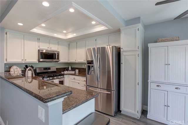 kitchen featuring dark stone counters, stainless steel appliances, light wood-style floors, white cabinets, and a peninsula