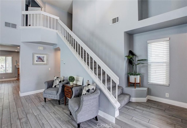 stairway with visible vents, wood finished floors, and a towering ceiling