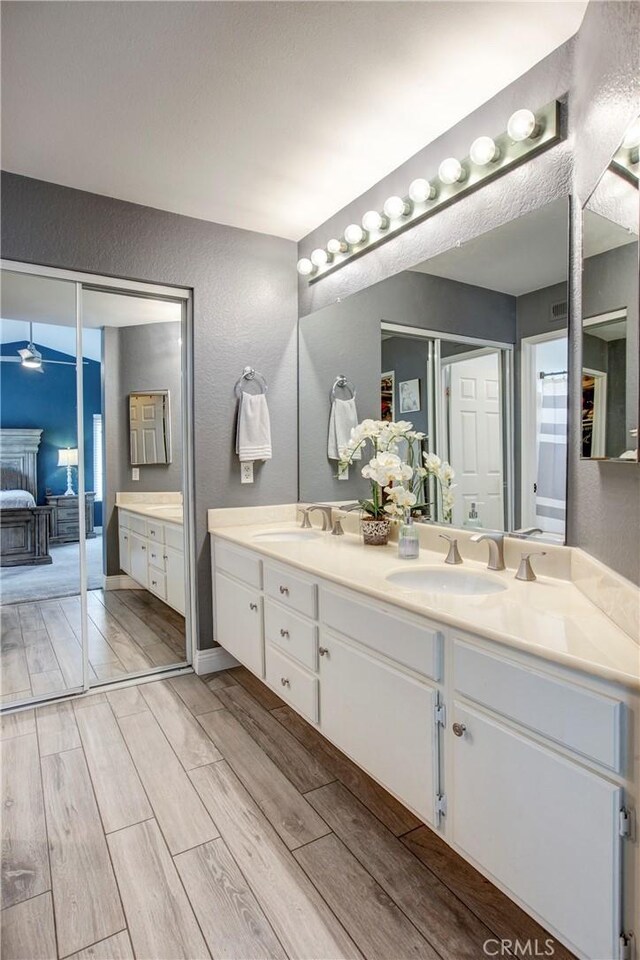 full bath with wood finished floors, double vanity, a textured wall, and a sink