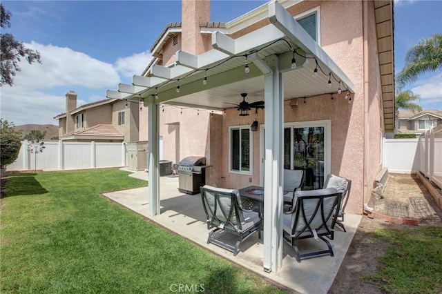 rear view of property with a fenced backyard, stucco siding, a yard, ceiling fan, and a patio area